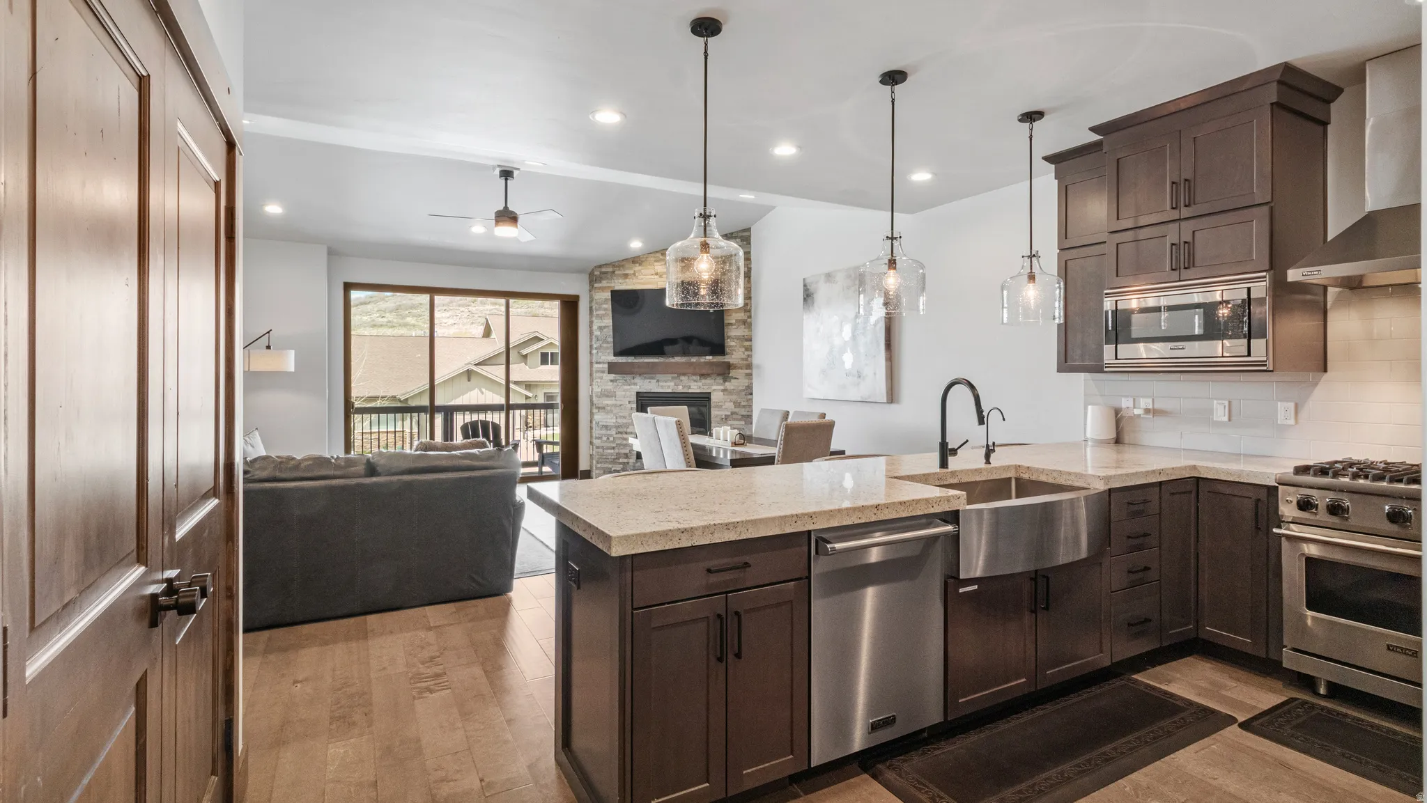 Kitchen with a fireplace, a peninsula, stainless steel appliances, dark wood finish cabinets, and light wood-type flooring
