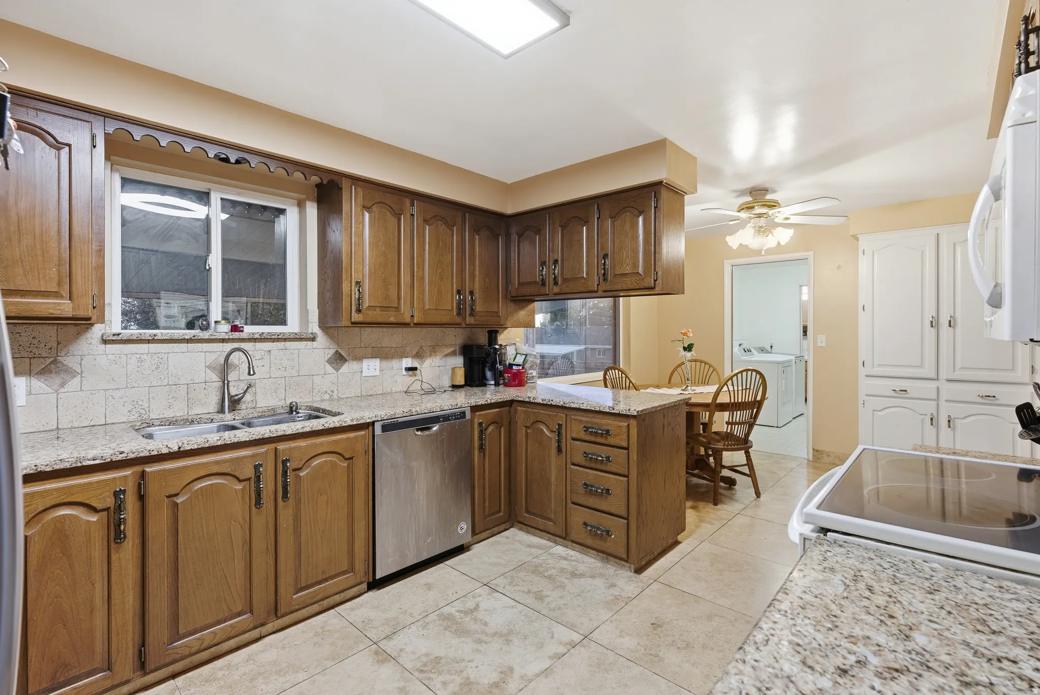 Kitchen with light stone counters, a peninsula, dishwasher, decorative backsplash, and white microwave