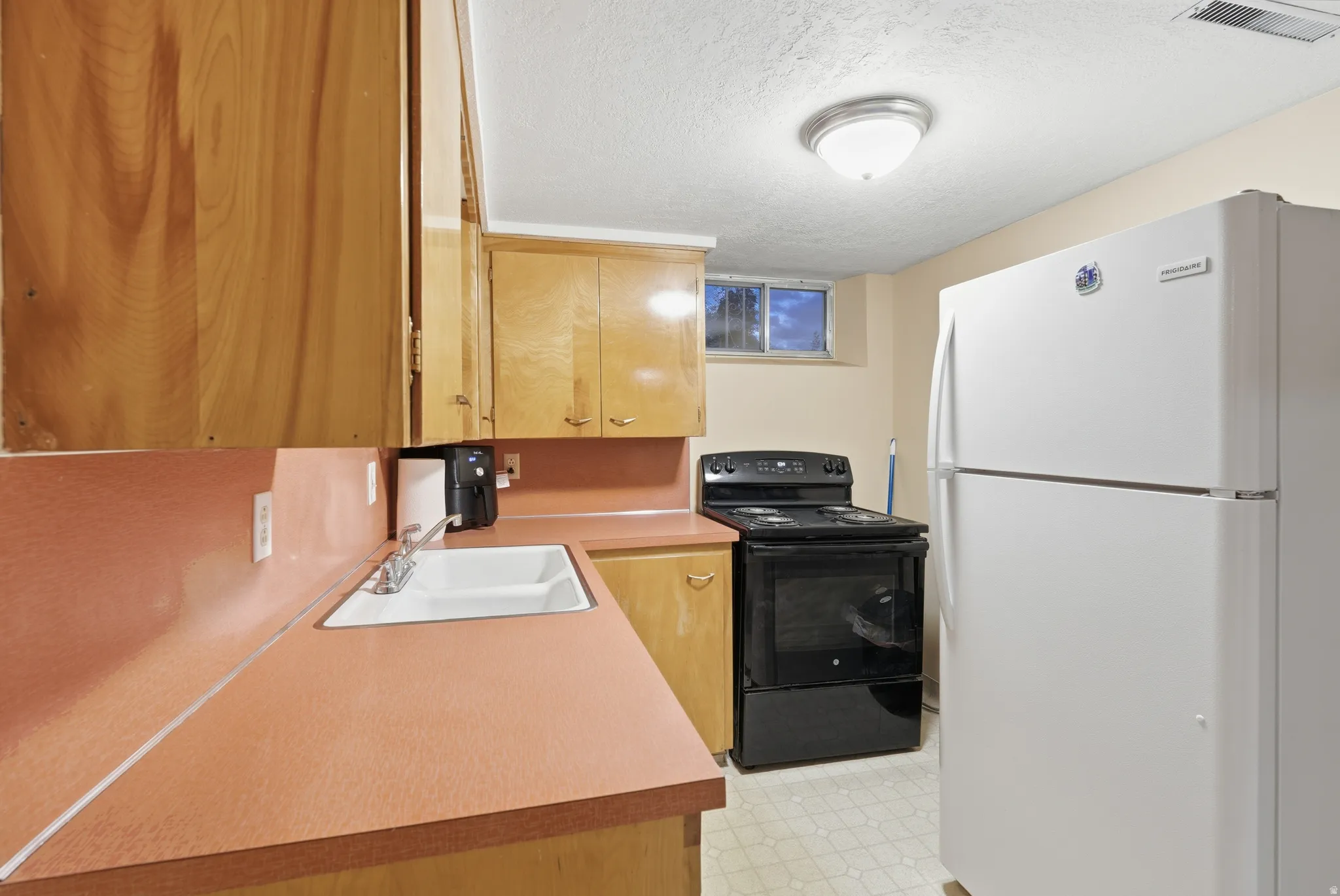 Kitchen with freestanding refrigerator, black electric range oven, a textured ceiling, light floors, and light countertops