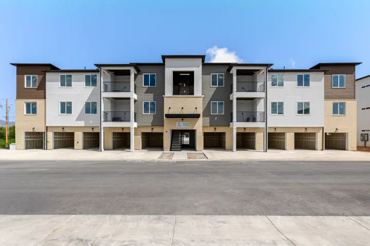 Modern multi-story facade featuring mixed-material siding, individual garage bays, multiple private balconies, and a central entry with exterior staircase