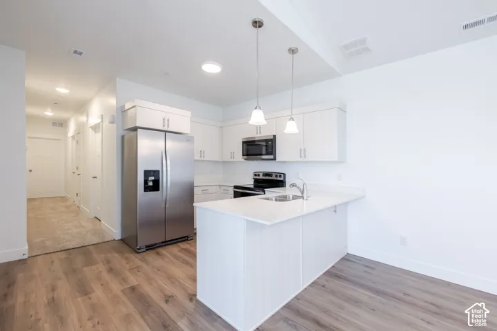 Kitchen featuring white cabinetry, wood-finish flooring, stainless steel appliances, a peninsula with stone-finish countertop, and pendant lighting