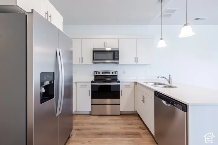 Kitchen featuring white cabinetry, solid-surface countertops, wood-finish flooring, stainless steel appliances, and dual pendant lighting