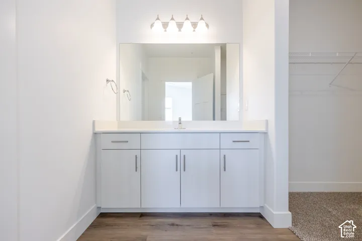Vanity featuring white cabinetry, a solid-surface countertop, an expansive wall-mounted mirror, four-bulb light fixture, and wood-finish flooring