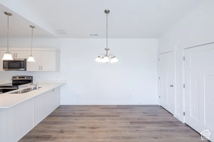 Kitchen featuring white cabinetry, quartz countertops, dual stainless steel sink, wood-finish flooring, and multi-light pendant fixtures