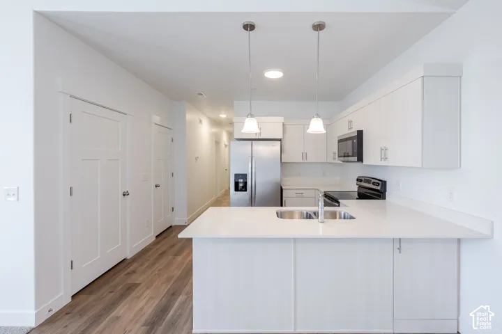 Kitchen featuring white cabinetry, quartz countertops, dual-basin stainless steel sink, wood-finish flooring, and pendant lighting