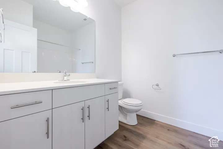 Bathroom featuring a light-toned cabinetry vanity with a solid-surface countertop, an integrated sink, a full-width mirror, and wood-finish flooring