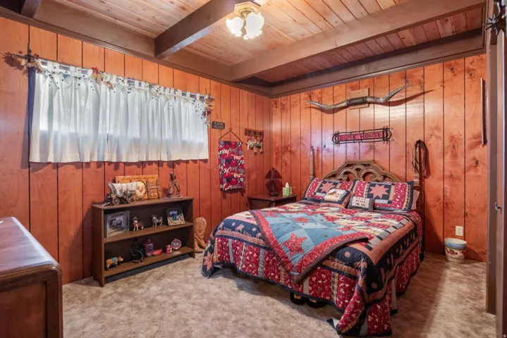 Carpeted bedroom featuring wooden walls and a wooden ceiling with exposed beams