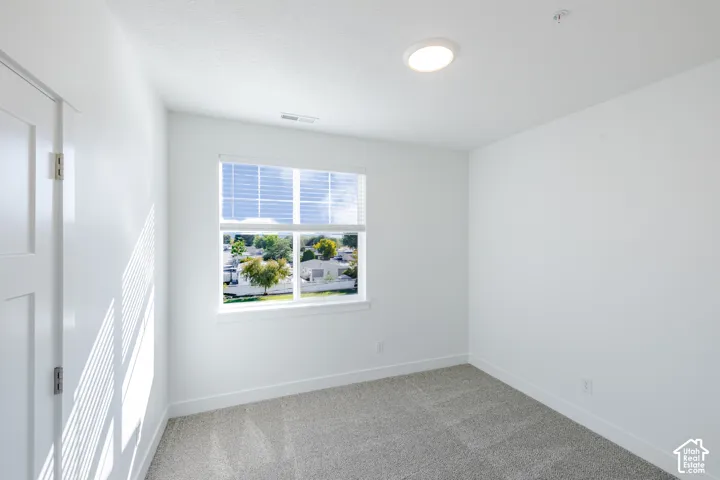 Neutral-toned interior featuring wall-to-wall carpeting, crisp white walls, a multi-pane window with integrated blinds, and a flush-mount overhead light fixture