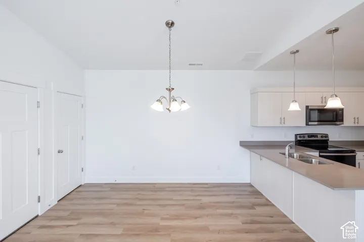 Open floor plan featuring wood-finish flooring, white cabinetry, solid-surface countertops, dual pendant lights, and a central chandelier