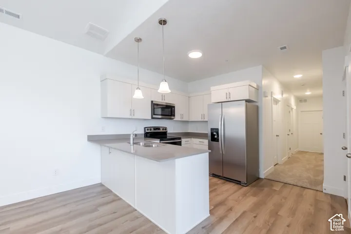 Kitchen featuring white cabinetry, solid-surface countertops, stainless steel appliances, wood-finish flooring, and pendant lighting