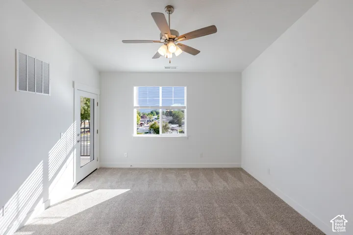Neutral-toned carpeted room featuring a ceiling fan with integrated lighting, a single window, and a glass-paned door