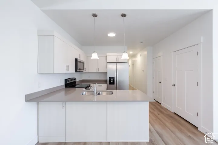 Kitchen featuring white shaker-style cabinetry, solid-surface countertops, dual stainless-steel sink, stainless-steel appliances, and wood-finish flooring