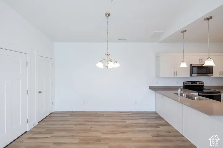 Kitchen featuring wood-finish flooring, white cabinetry, a solid-surface countertop, stainless steel appliances, and dual pendant lighting
