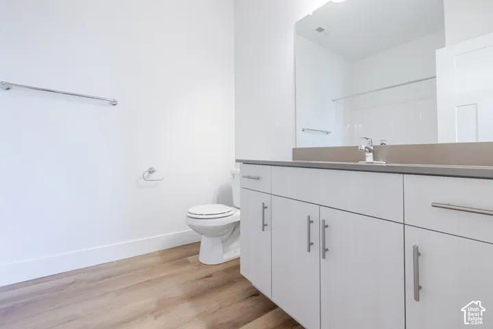 Bathroom vanity with wood-finish cabinetry, solid surface countertop, chrome hardware, integrated sink, and full-width wall mirror over wood-finish flooring