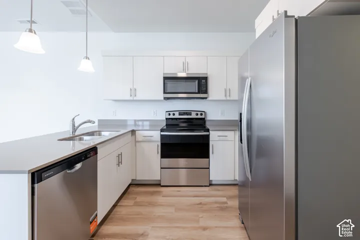 Kitchen featuring white cabinetry, solid-surface countertops, wood-finish flooring, stainless steel appliances, and dual pendant lighting