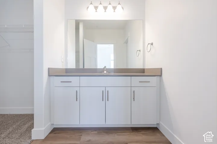 White vanity cabinetry featuring satin-finish hardware, solid-surface countertop with an integrated sink, full-width wall mirror, and four-bulb light fixture