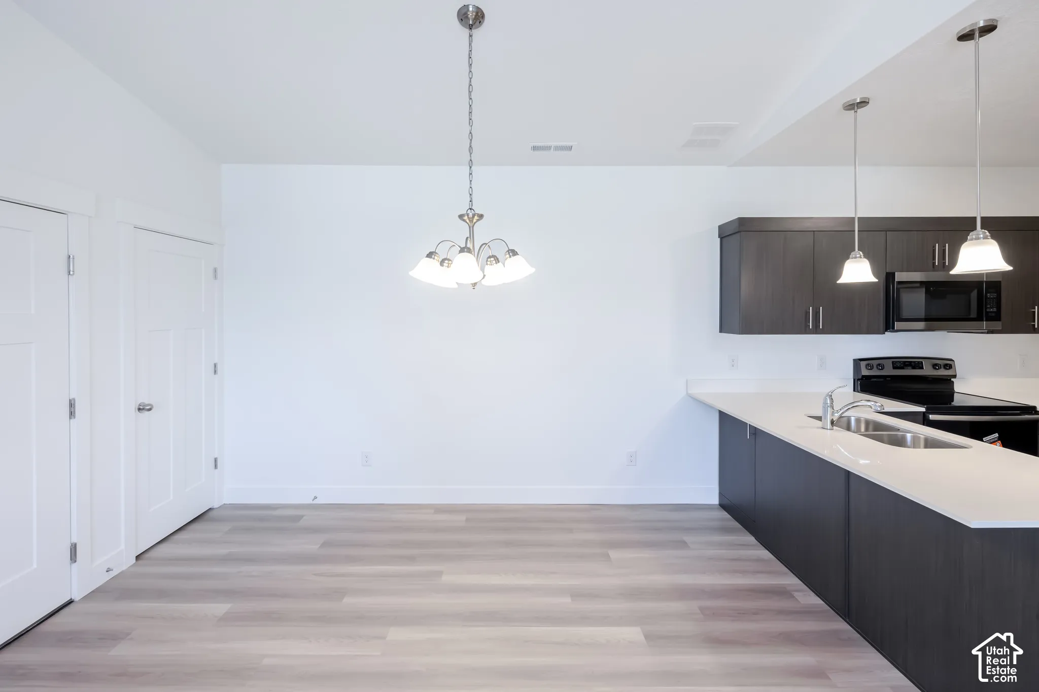 Open-concept area featuring light-toned wood-finish flooring, dark cabinetry with satin nickel hardware, solid-surface countertops, dual-pendant lighting, and a multi-arm chandelier