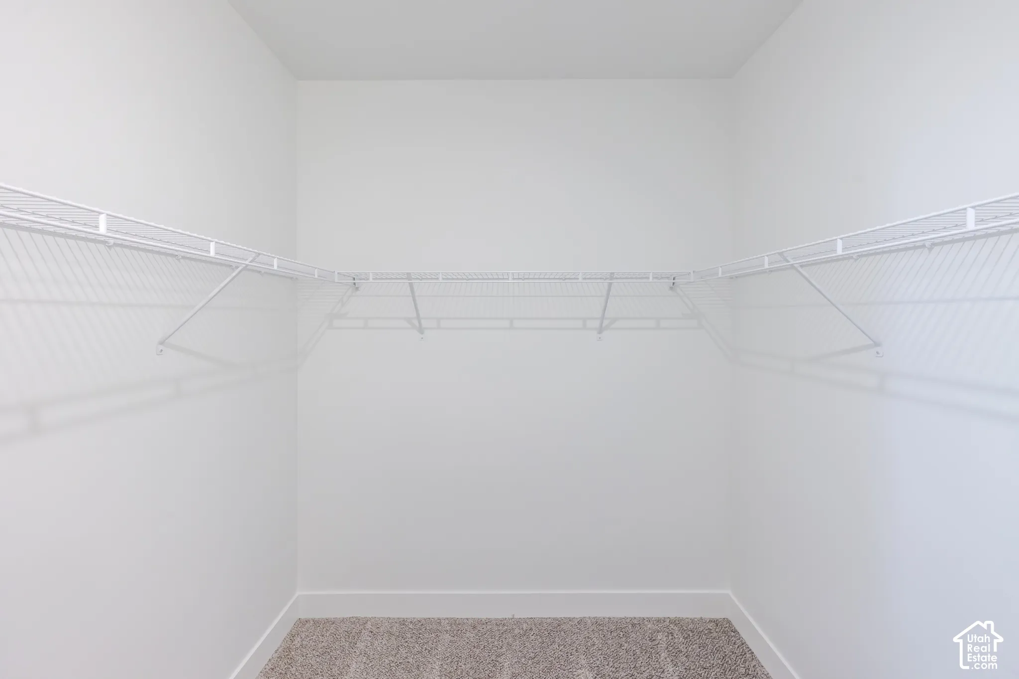 Walk-in storage space featuring neutral carpeting and wrap-around white wire shelving