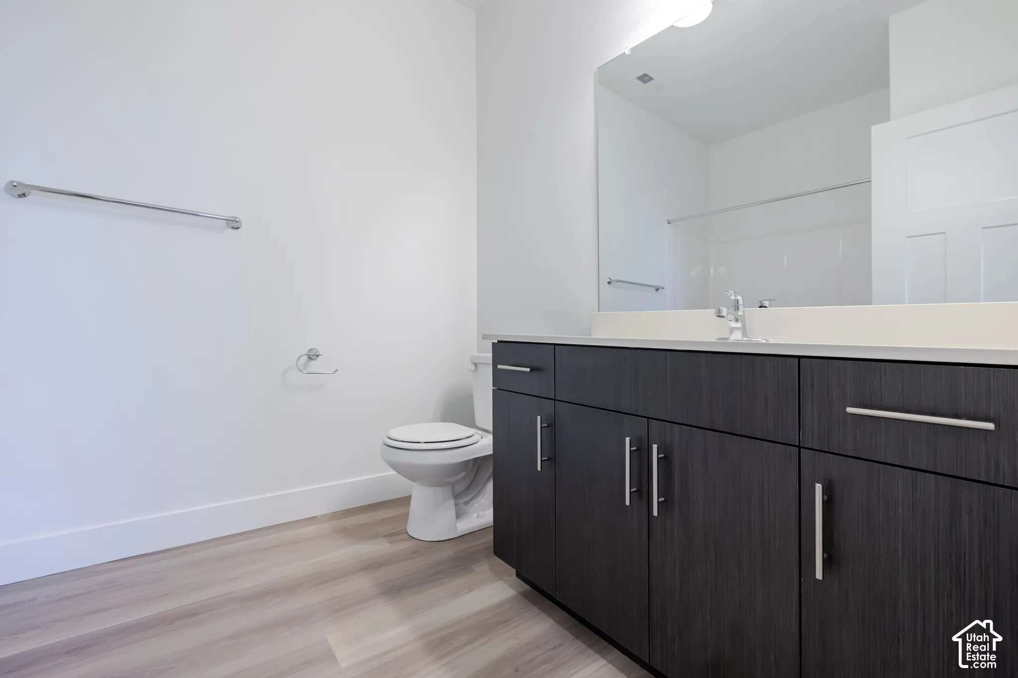 Bathroom featuring a dark wood-finish vanity with a light-toned countertop, large rectangular wall-mounted mirror, and light-toned wood-finish flooring