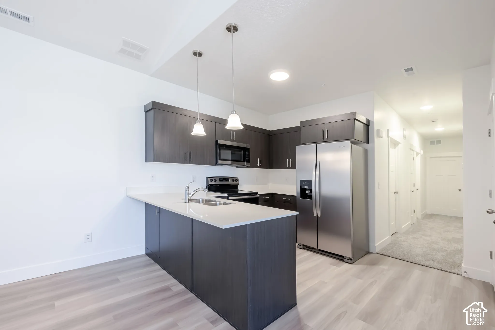 Kitchen featuring dark-finish cabinetry, quartz countertops, stainless steel appliances, a peninsula breakfast bar, and pendant lighting