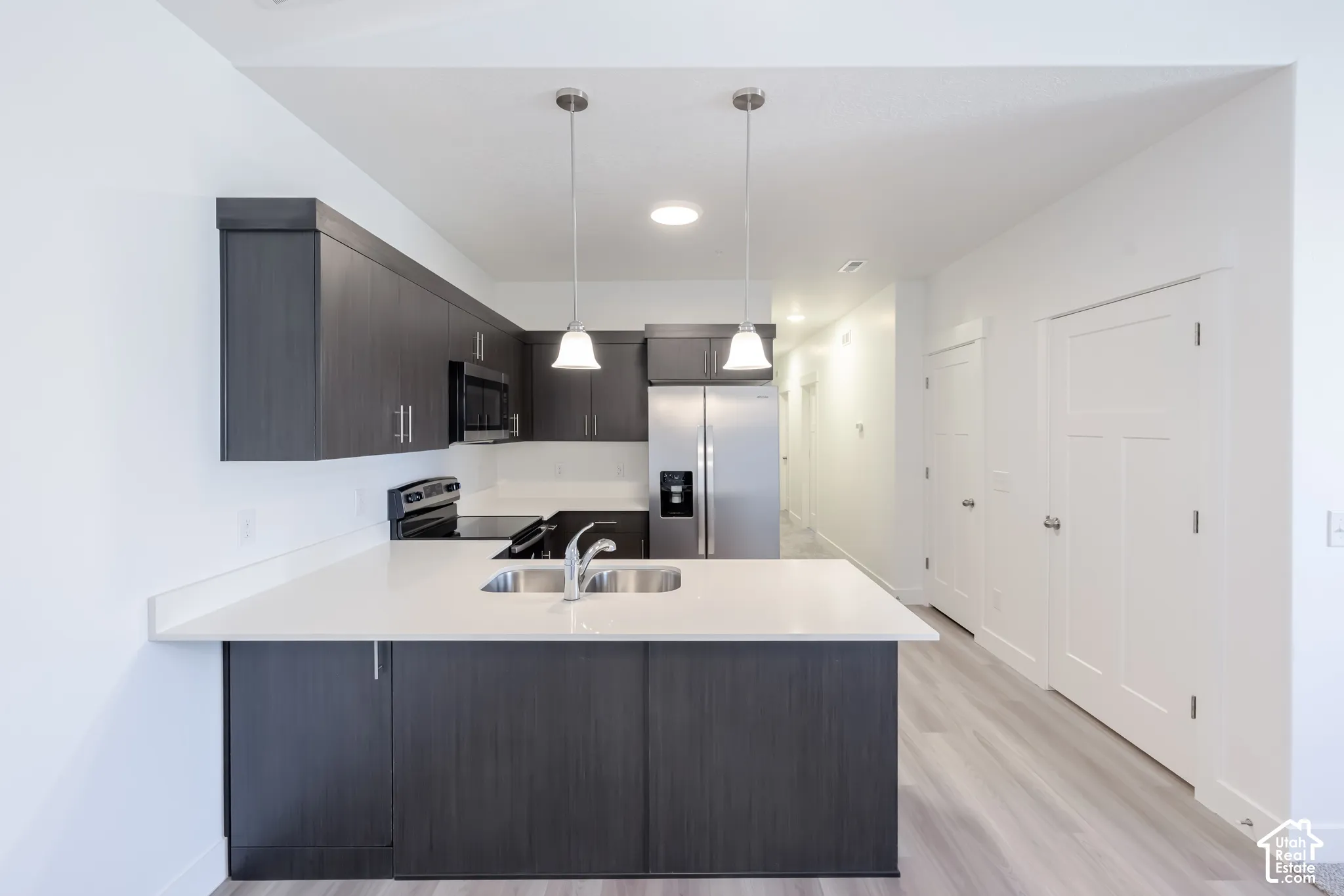 Kitchen featuring dark-finish cabinetry, solid-surface countertops, stainless steel appliances, dual pendant lighting, and wood-finish flooring