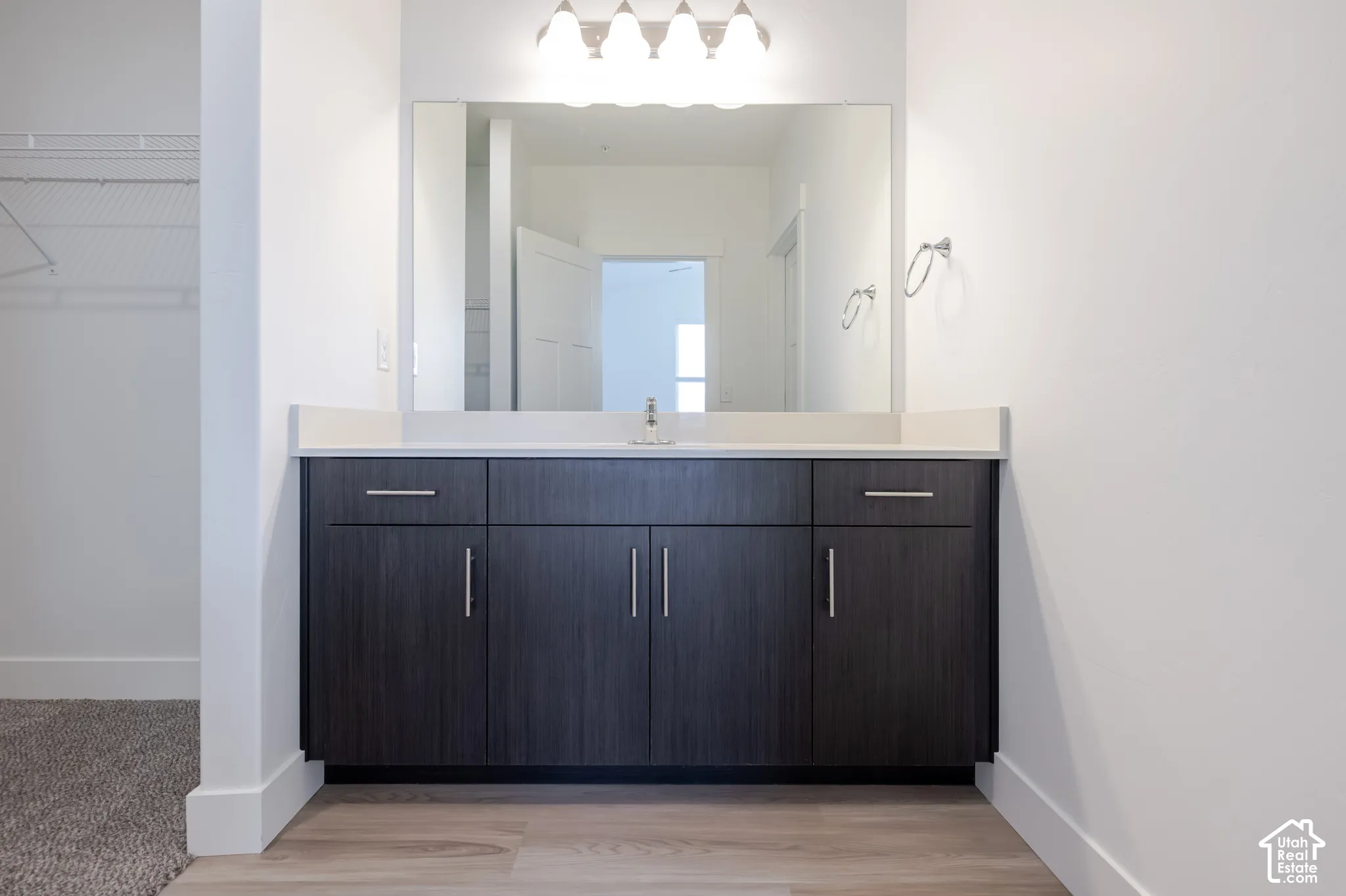 Dark wood-finish cabinetry, countertop with integrated sink, large wall-mounted mirror, four-bulb light fixture, and chrome-finished hardware