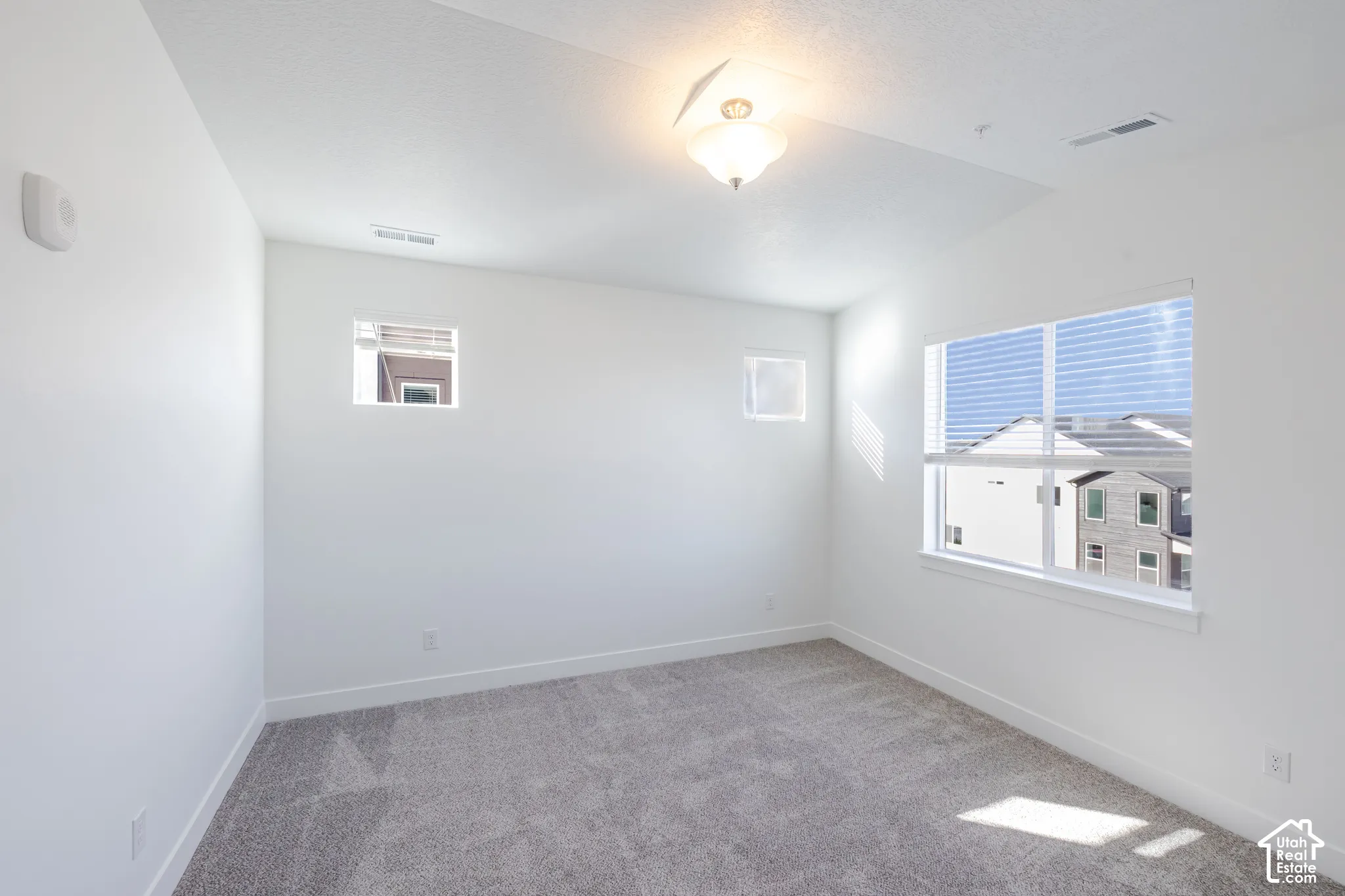 Room featuring high ceilings, neutral wall-to-wall carpeting, large picture window, two clerestory windows, and a flush-mount ceiling fixture