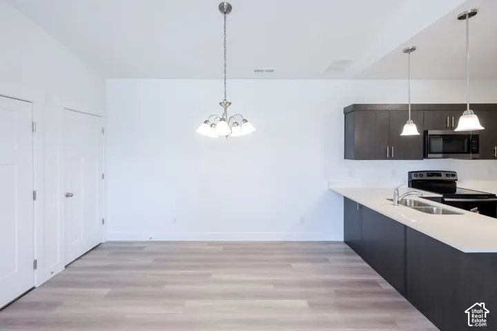 Open-concept area featuring light-toned wood-finish flooring, dark cabinetry with satin nickel hardware, solid-surface countertops, dual-pendant lighting, and a multi-arm chandelier