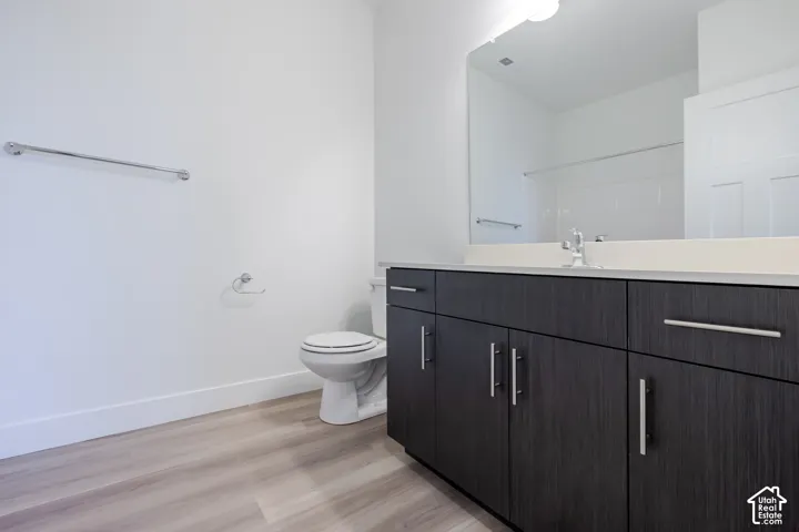 Bathroom featuring a dark wood-finish vanity with a light-toned countertop, large rectangular wall-mounted mirror, and light-toned wood-finish flooring