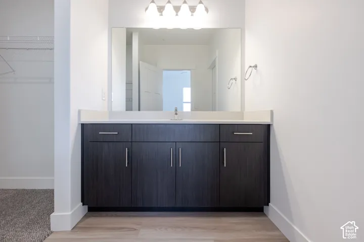 Dark wood-finish cabinetry, countertop with integrated sink, large wall-mounted mirror, four-bulb light fixture, and chrome-finished hardware