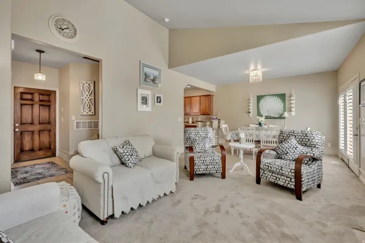 Carpeted living area featuring vaulted ceilings, a decorative crystal chandelier, and a paneled wooden entry door with an overhead pendant light