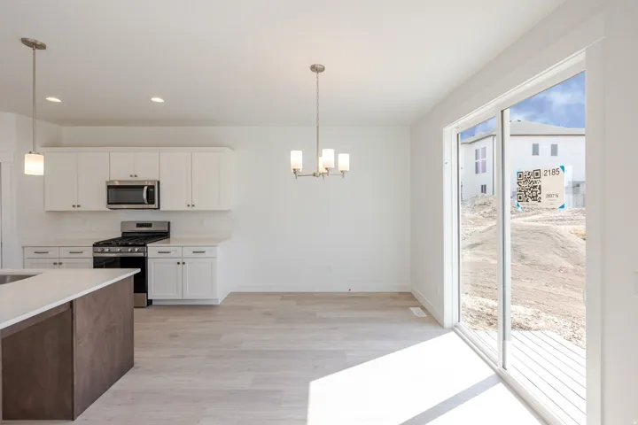 White cabinetry with stainless steel appliances, light wood-finish flooring, and a sliding glass door
