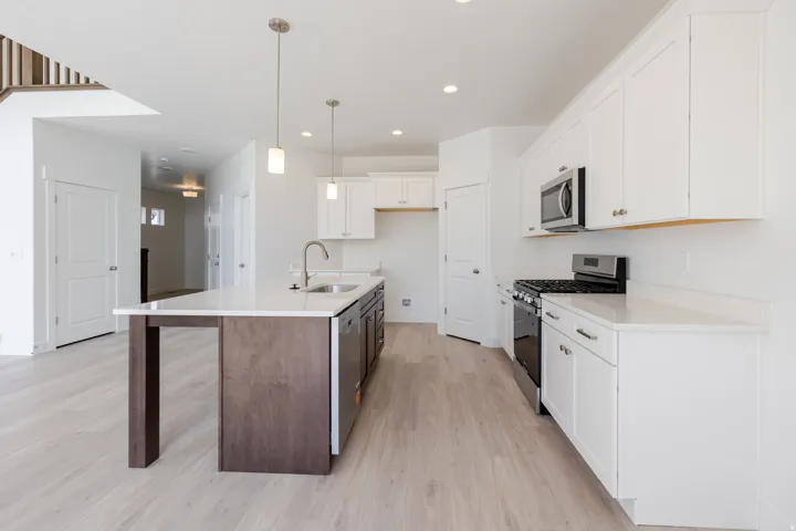 Modern kitchen featuring an island with a built-in sink, white cabinetry with silver hardware, a stainless steel gas range, and wood-finish flooring