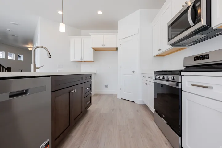 Stainless steel appliances, white cabinetry, dark wood-finish island, light wood-finish flooring, and a contemporary pendant light fixture