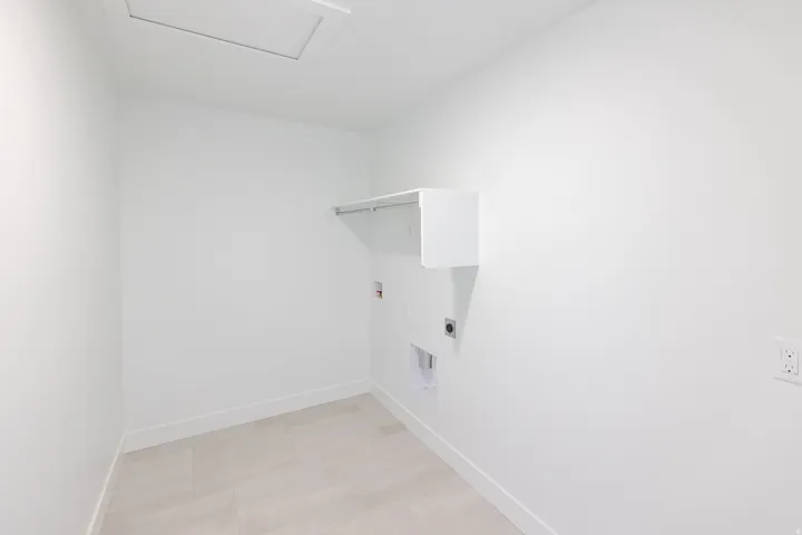 Utility room featuring light-toned flooring, white walls, and a built-in shelf with a hanging rod