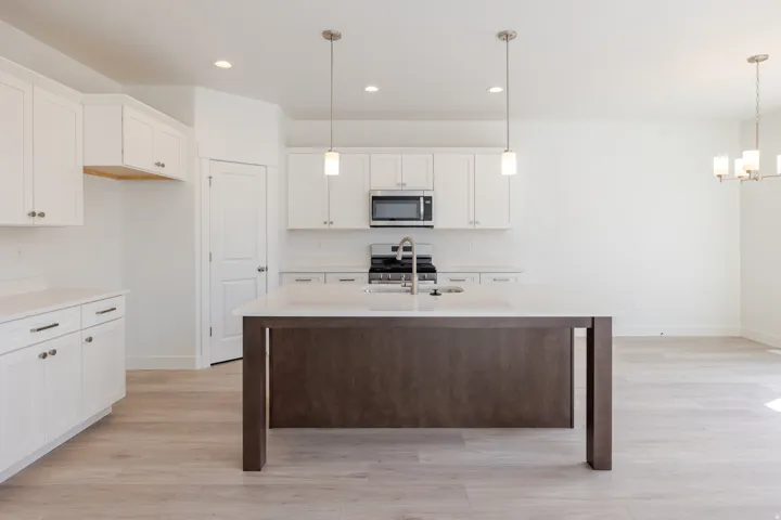White shaker cabinetry, light wood-finish flooring, recessed lighting, central island with sink, and stainless steel appliances
