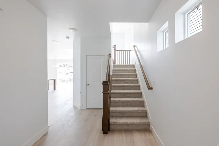 Entryway featuring wood-finish flooring, a carpeted staircase with wood handrails, and upper wall windows