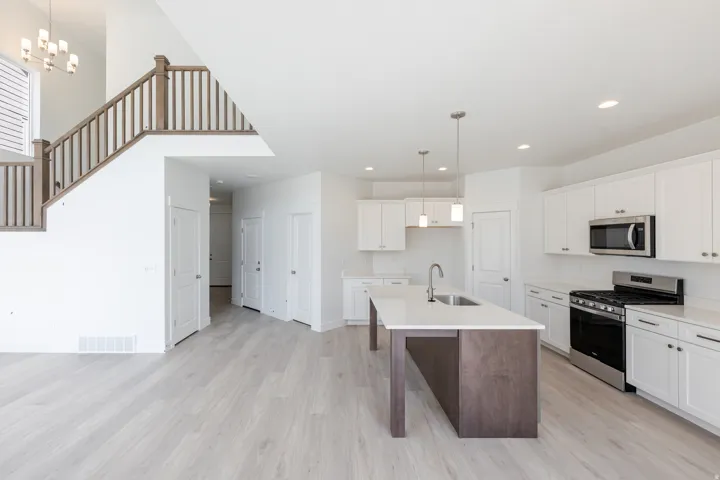 Open-concept kitchen and dining area featuring white cabinetry, stainless steel appliances including a dual-fuel range and built-in microwave, an island with contrasting wood-finish base, wood-finish flooring throughout, and recessed ceiling lighting
