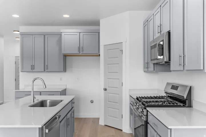 Modern kitchen featuring light gray cabinetry, stainless steel appliances, white countertops, and light wood-finish flooring