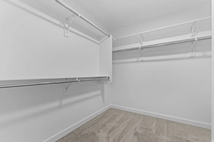 Spacious closet featuring white painted walls, white shelving, and chrome hanging rods
