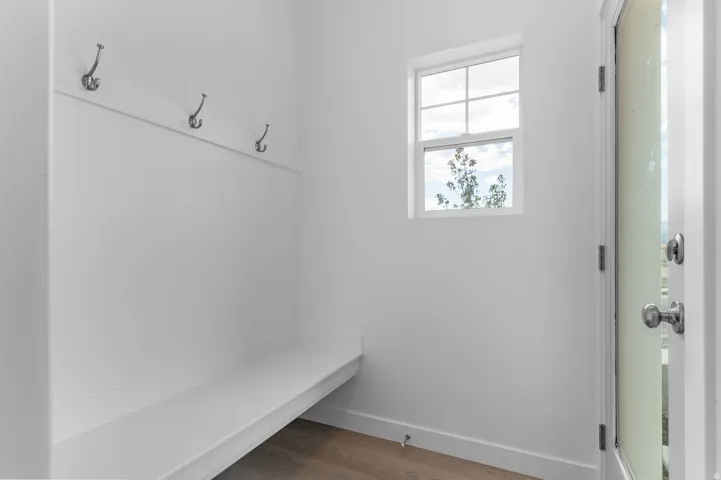 Built-in bench seating with wall-mounted hooks, transom window, wood-finish flooring, and a white exterior door with glass paneling