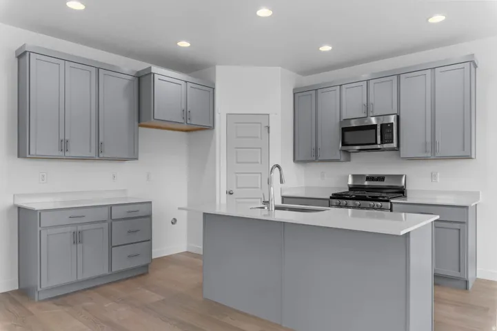 Modern kitchen featuring gray shaker-style cabinetry, light countertops, stainless steel appliances, a center island with an undermount sink, and recessed lighting
