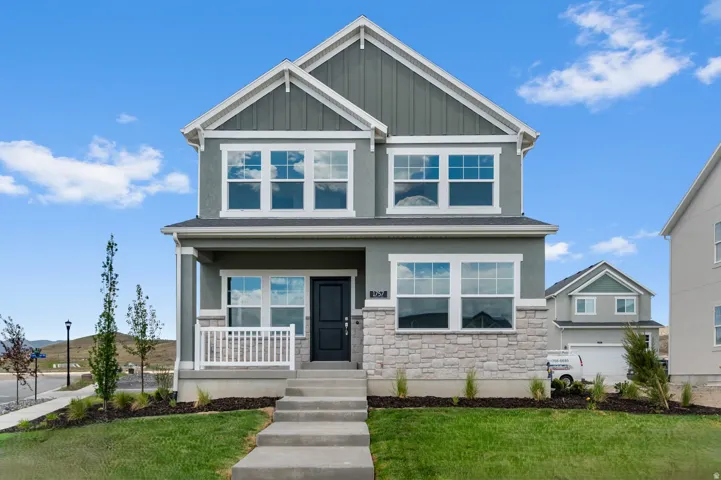 Modern craftsman-style facade featuring gray siding, stone accents, a covered porch with white railings, and a dark entry door