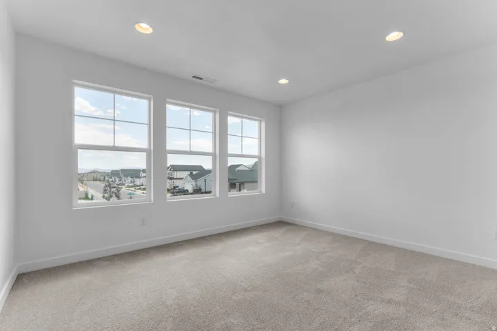 Bright room featuring three large windows, recessed ceiling lighting, light gray carpeting, and white baseboards