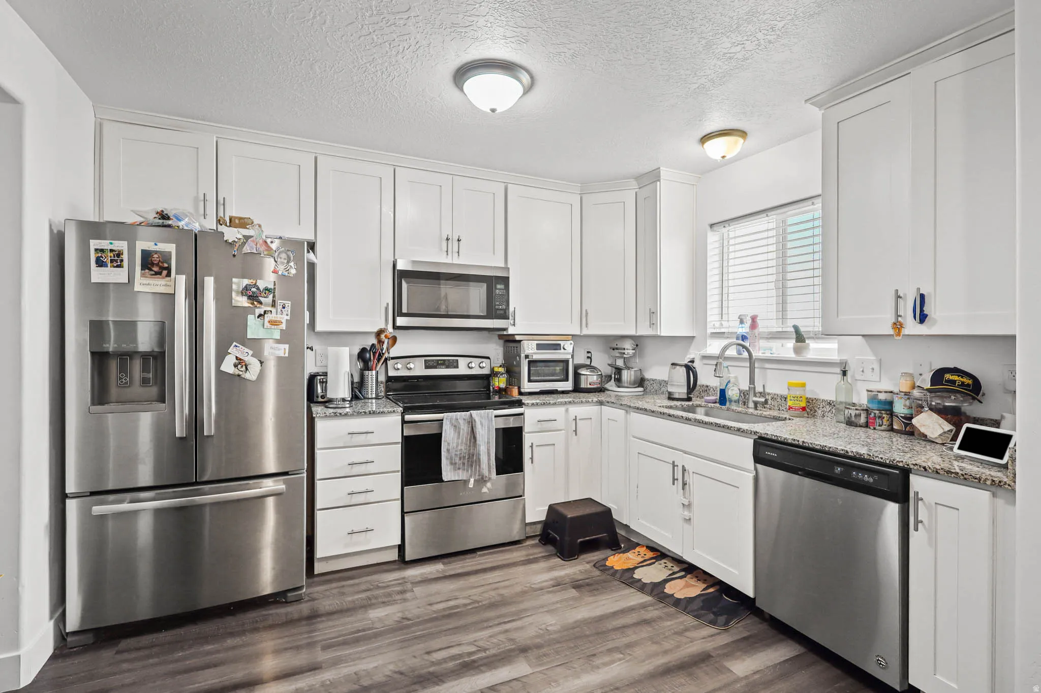 Kitchen with stainless steel appliances, white cabinetry, light stone countertops, a textured ceiling, and dark wood-style floors