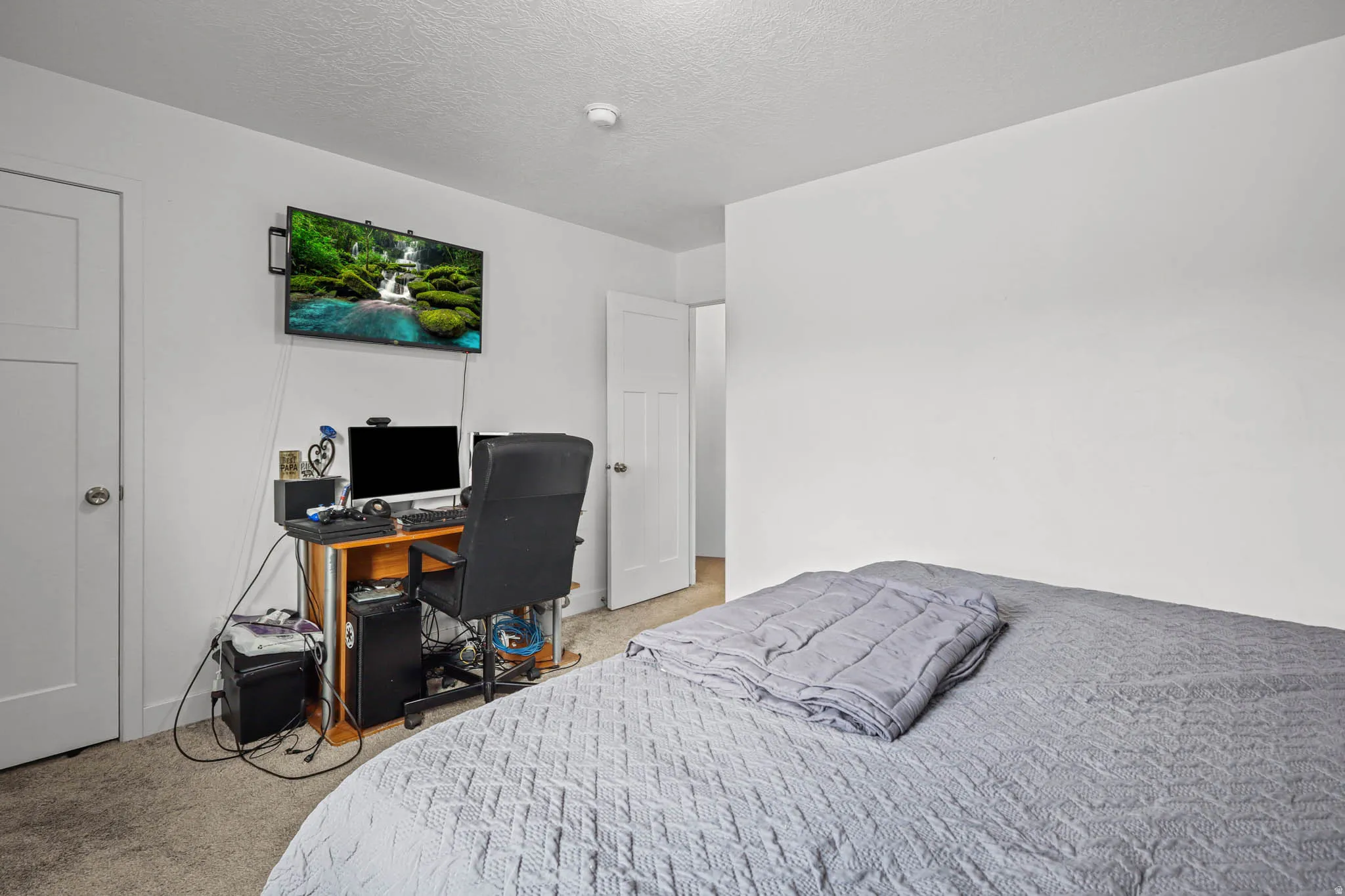Bedroom featuring light colored carpet, a desk, and a textured ceiling