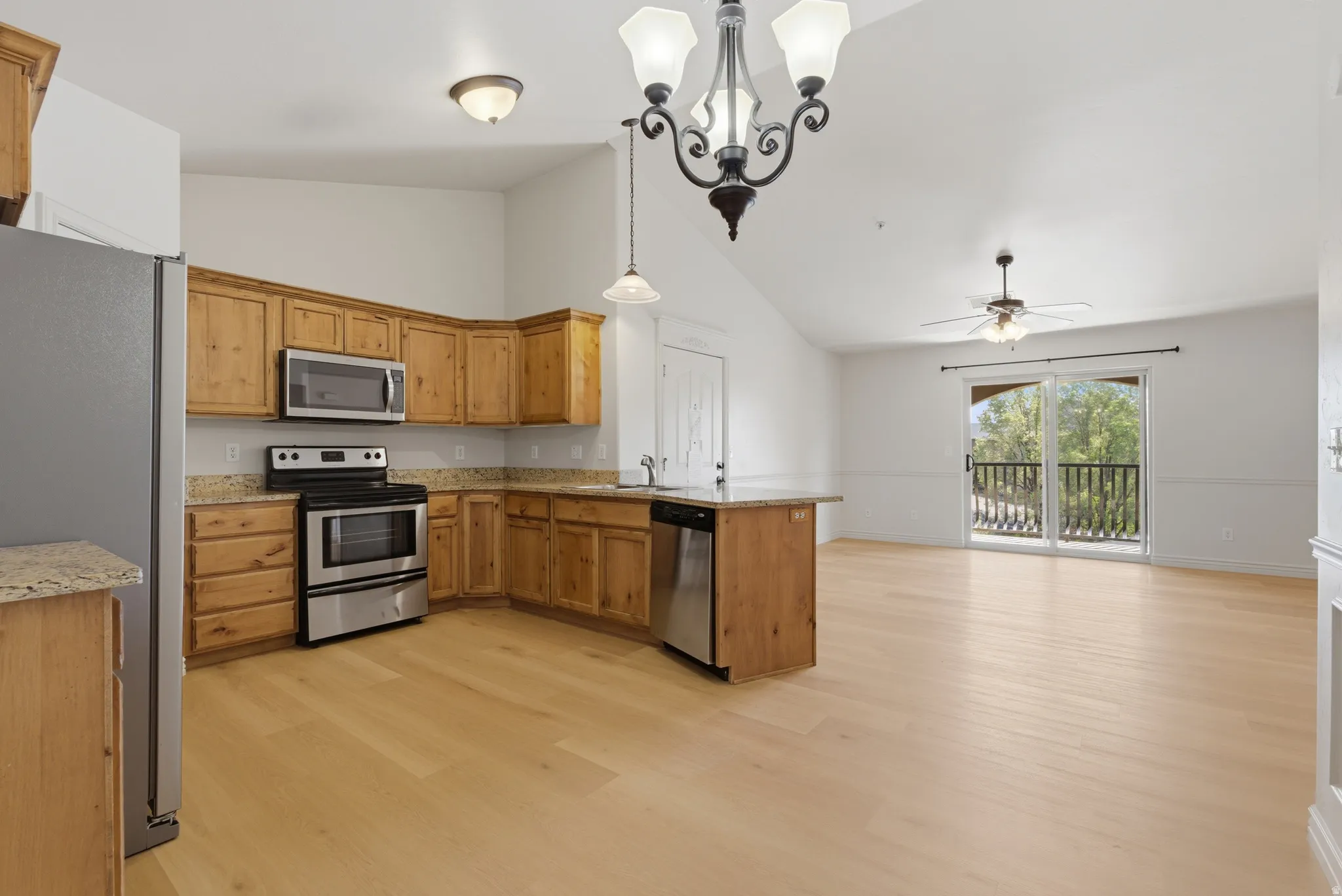 Kitchen with stainless steel appliances, a chandelier, light stone countertops, open floor plan, and a peninsula