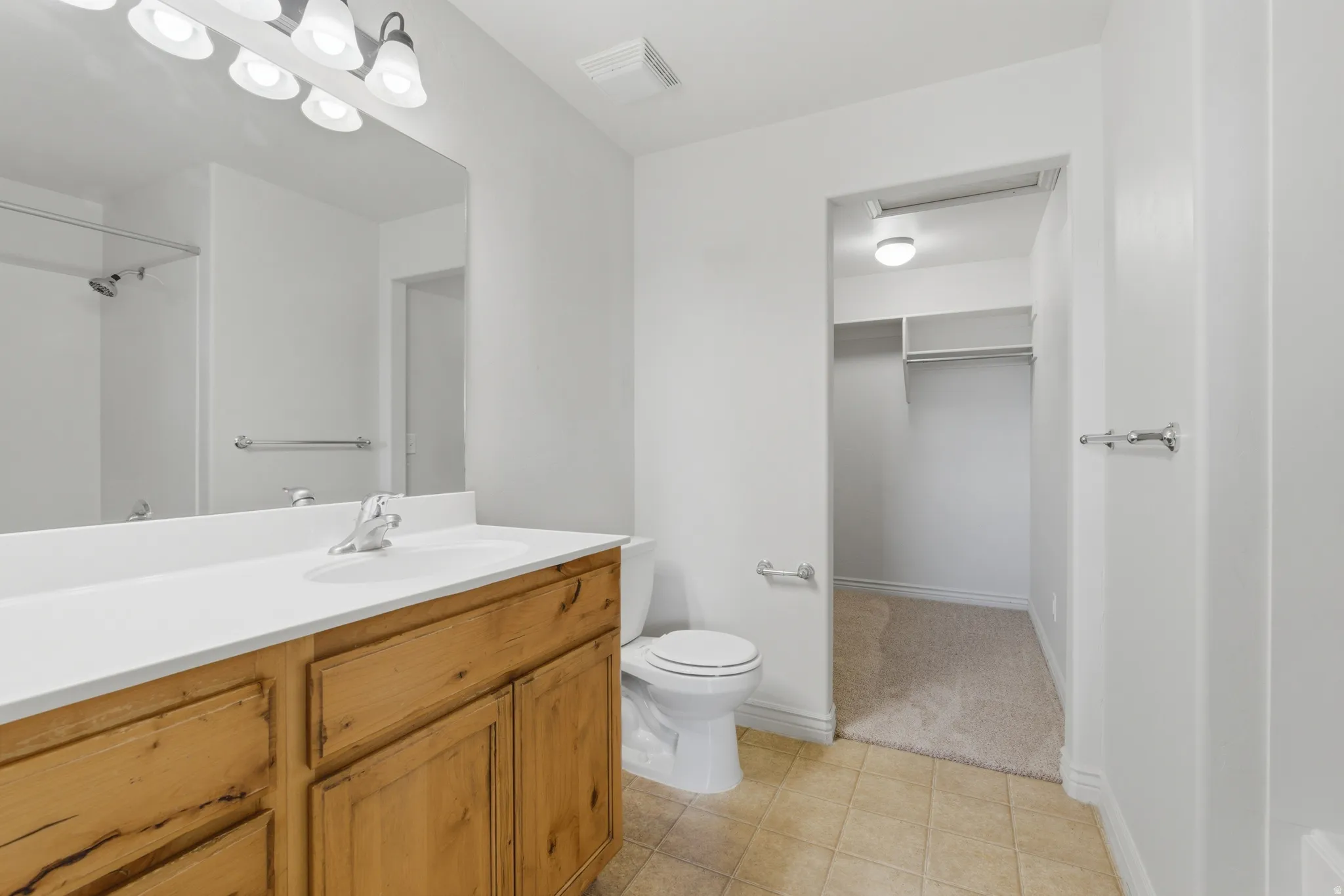 Bathroom featuring vanity, a walk in closet, light tile patterned floors, and a shower