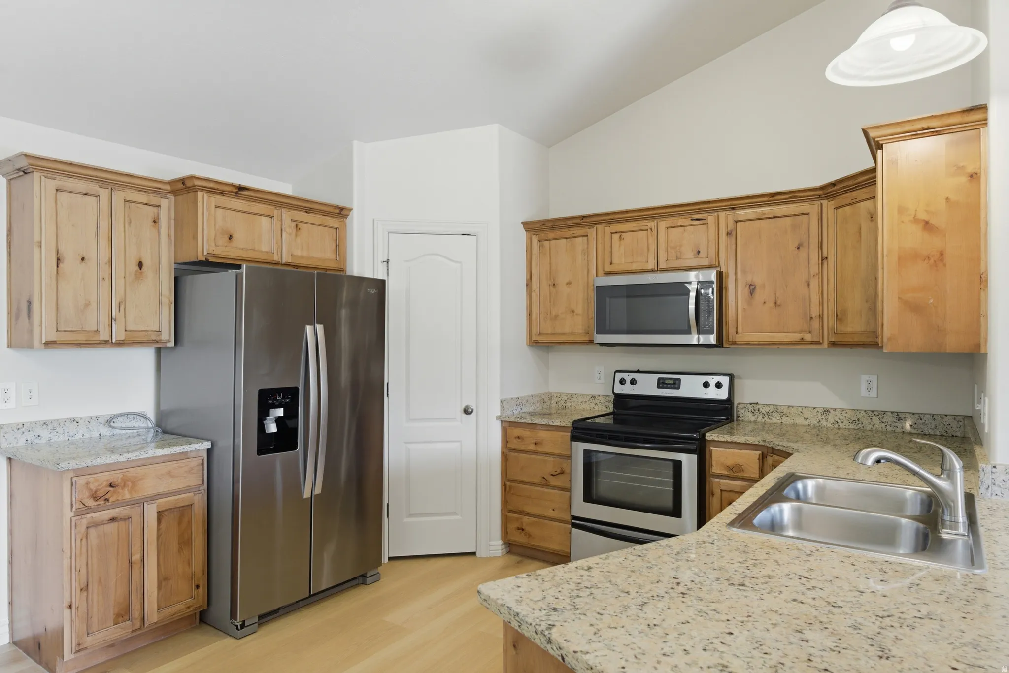 Kitchen featuring stainless steel appliances, lofted ceiling, light stone countertops, and light wood finished floors