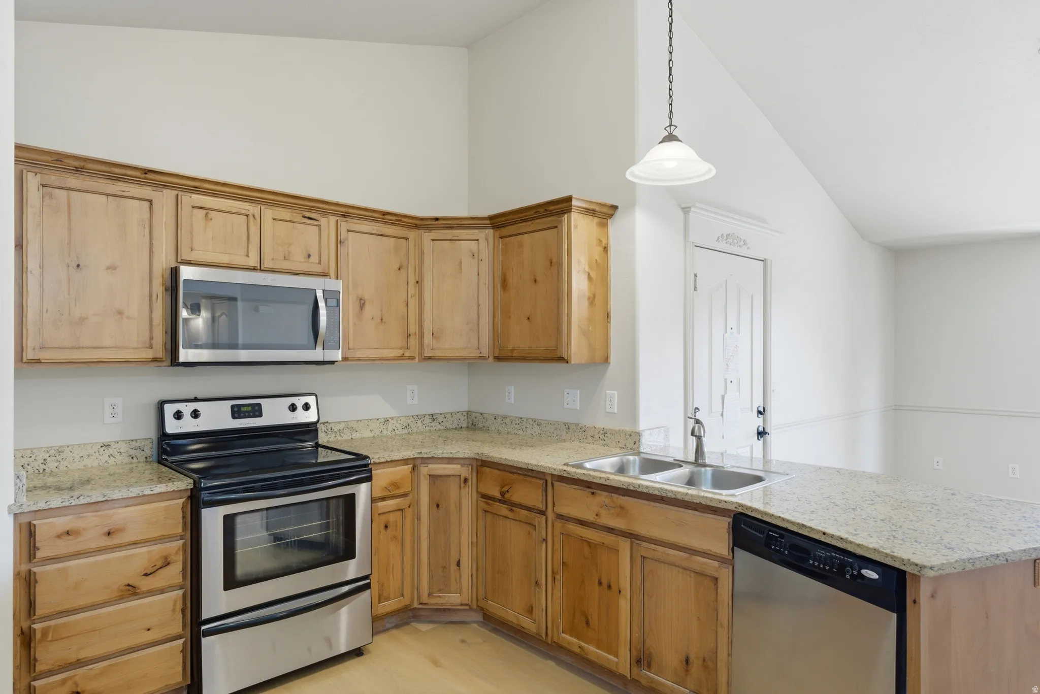 Kitchen featuring stainless steel appliances, a peninsula, light stone counters, hanging light fixtures, and vaulted ceiling